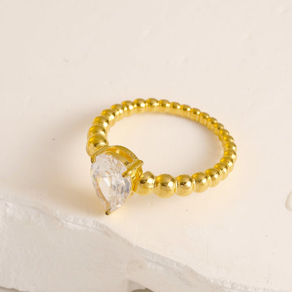 Bague dorée avec perles blanches et petit cœur, posée sur fond blanc