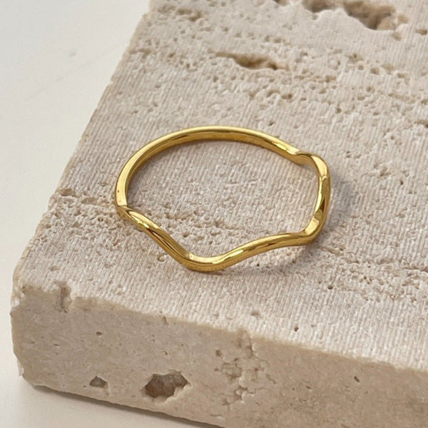 Bague dorée fine aux courbes fluides et minimalistes, présentée sur fond blanc