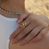  Bague dorée au design courbé et sculptural, avec finition lisse et brillante, présentée sur fond blanc