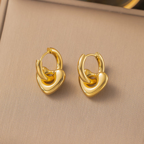 Boucles d’oreilles dorées en forme de cœur bombé avec anneau épais, portées à l’oreille.