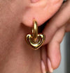 Boucles d’oreilles dorées en forme de cœur bombé avec anneau épais, portées à l’oreille.