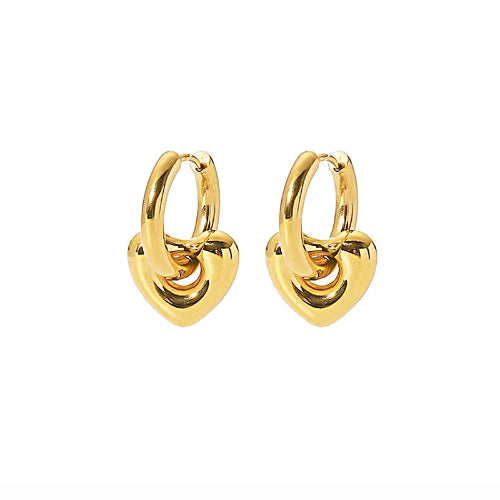 Boucles d’oreilles dorées en forme de cœur bombé avec anneau épais, portées à l’oreille.