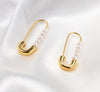Boucles d’oreilles dorées en forme d’épingle décorées de perles blanches, posées sur tissu satiné