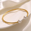 Bracelet jonc doré à l’or 18k avec deux perles blanches aux extrémités, posé sur un coussin rouge.