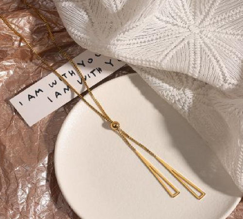 Collier doré 18k avec double pendentif triangle ajouré suspendu à une chaîne fine avec bille centrale.