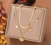 Collier triple doré avec pendentif turquoise et breloques étoiles, présenté sur un coussin beige.