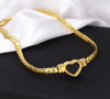 Collier doré rigide à maillons plats avec pendentif cœur ouvert, présenté sur fond blanc et noir.