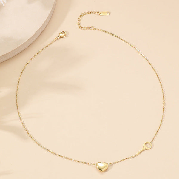 Collier doré avec pendentif en forme de cœur et petite clé assortie, présenté sur fond blanc