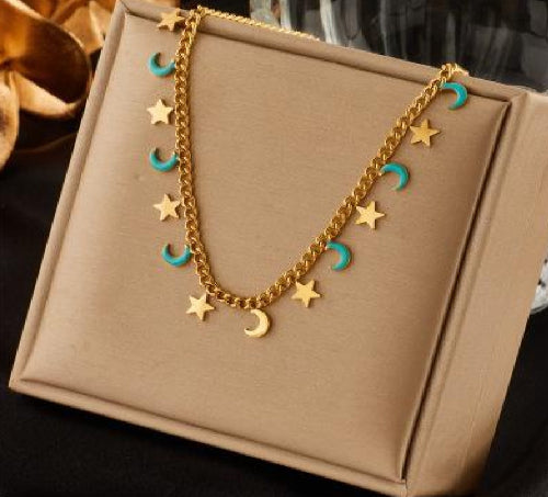 Collier doré avec pendentifs lunes turquoise et étoiles dorées, présenté sur un coussin beige.
