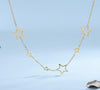 Collier doré avec étoiles ajourées de différentes tailles, sur fond bleu pastel.