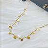 Collier doré 18k avec pampilles rondes plates accrochées à une fine chaîne, posé sur fond blanc.