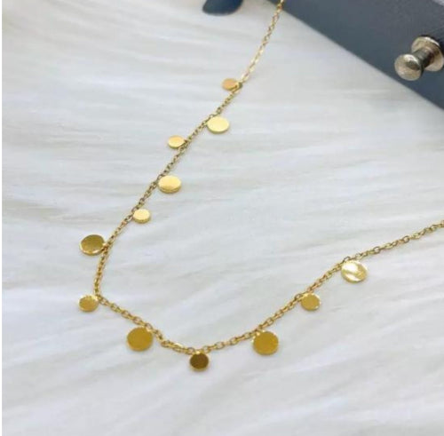 Collier doré 18k avec pampilles rondes plates accrochées à une fine chaîne, posé sur fond blanc.