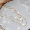 Collier doré à deux rangs avec petits pendentifs carrés, style délicat et moderne, présenté sur fond blanc