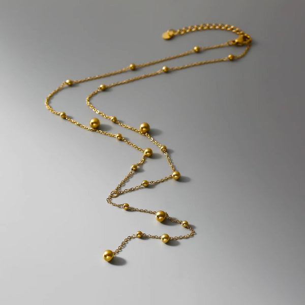 Collier en Y doré avec petites pampilles arrondies suspendues sur une chaîne fine, présenté sur fond blanc