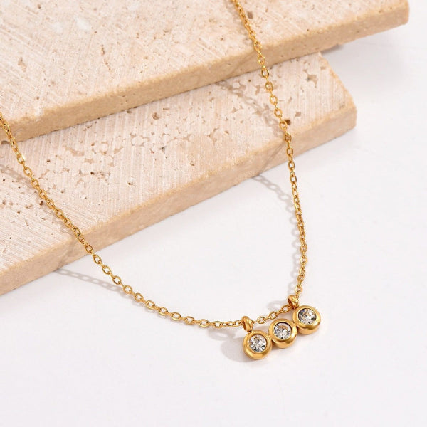 Collier doré avec trois zirconias alignés sur une chaîne fine, présenté sur fond blanc