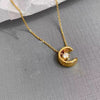 Collier doré avec pendentif en forme de lune et petite pierre brillante, présenté sur fond blanc