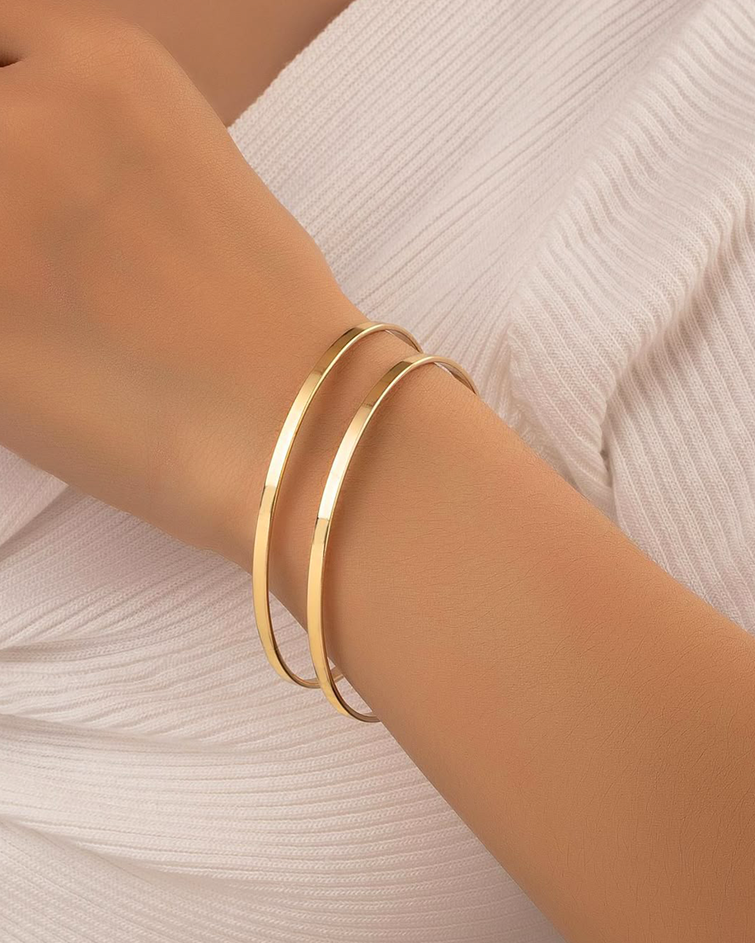 close up of two gold bracelets on model