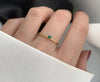 Bague fine dorée avec pierre verte éclatante, photographiée sur fond blanc